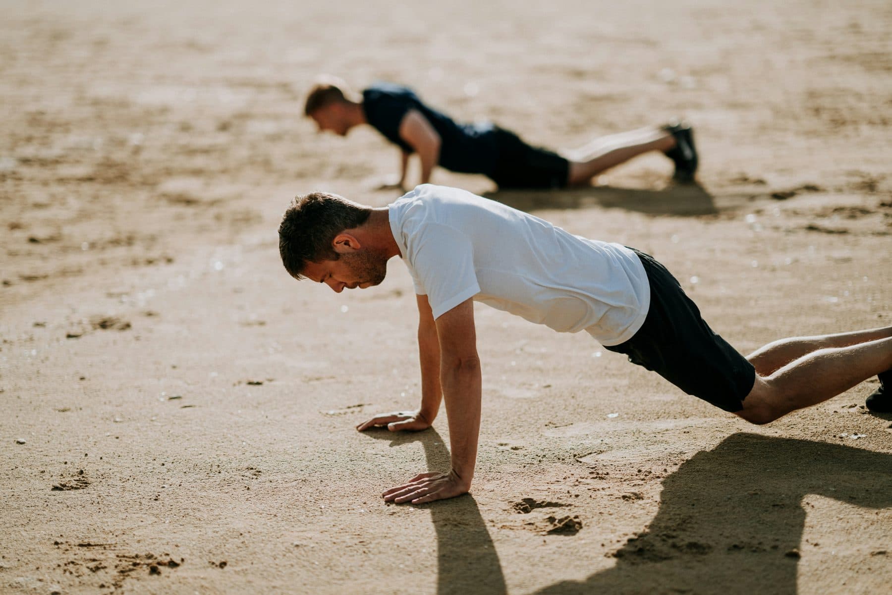 Two people exercising together on a beach.